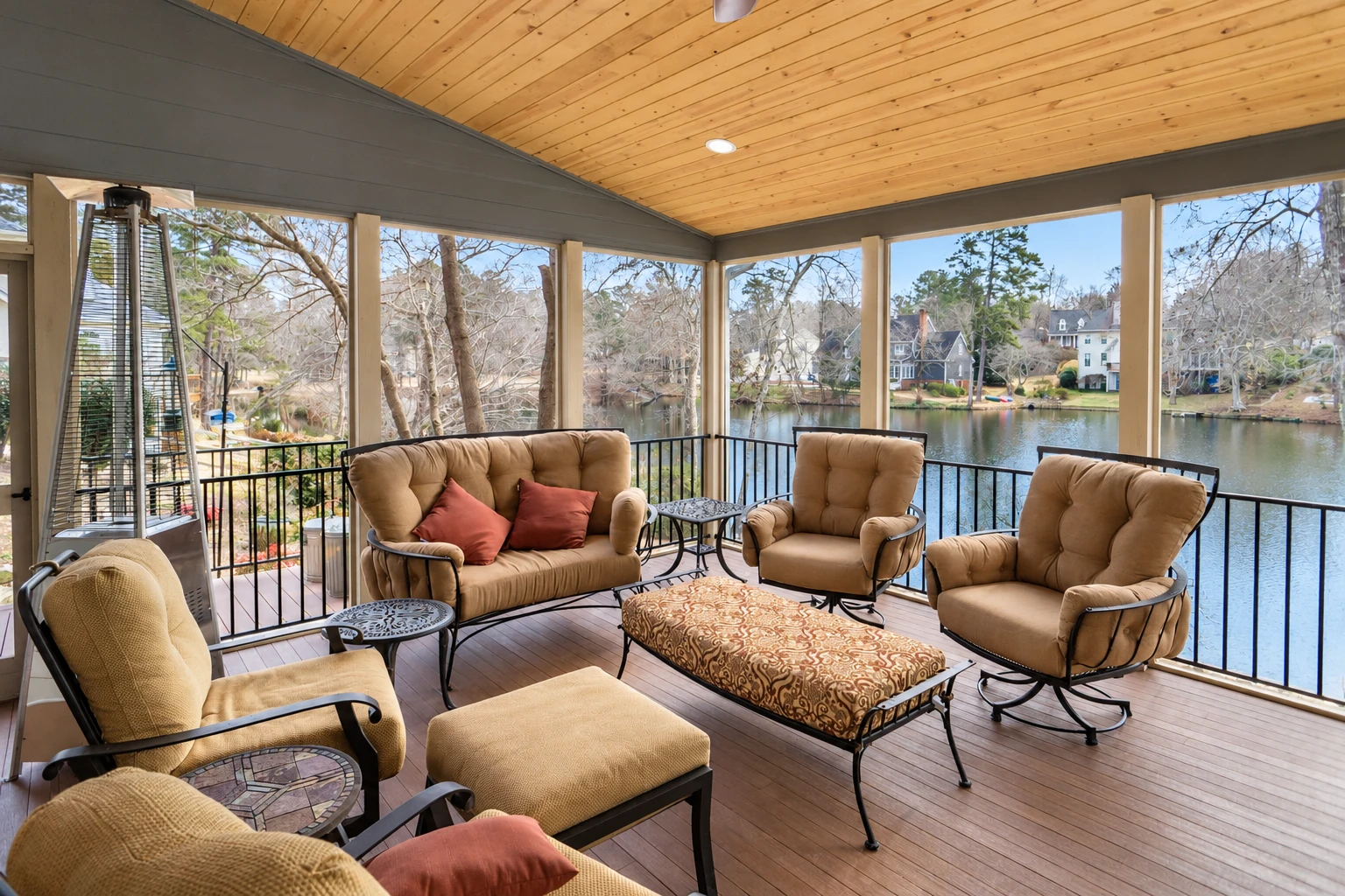 Screened sunroom with a wood-plank ceiling, cushioned seating, and views across a lake.