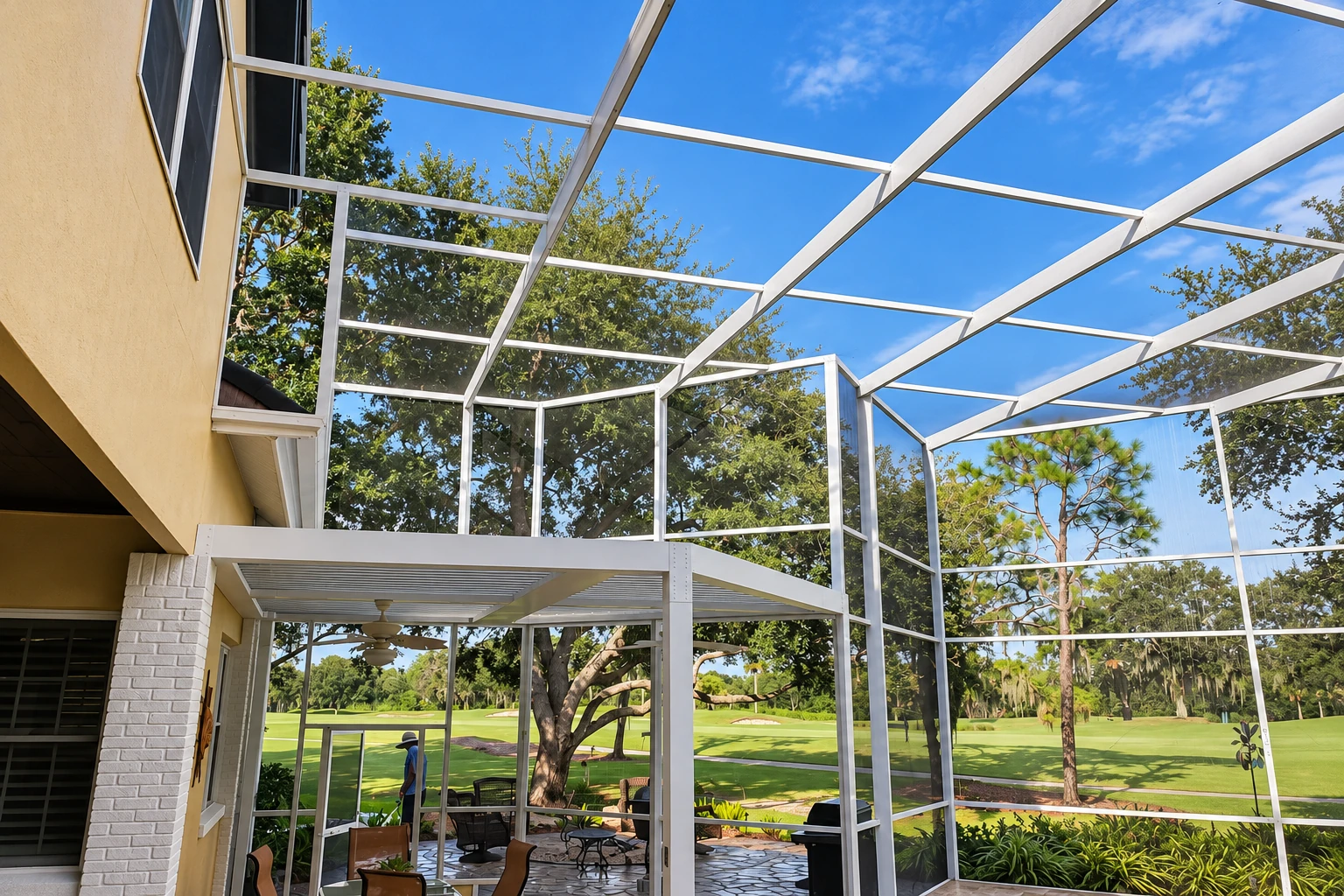 A large screen room with a white metal frame encloses a patio, opening views toward trees and a green lawn.