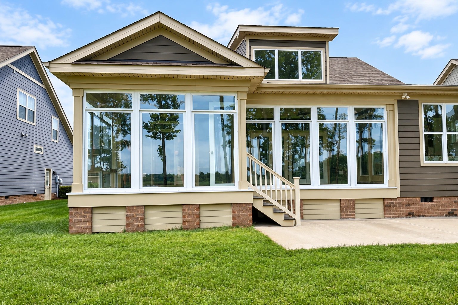 House exterior with a large beige sunroom addition, broad white-framed windows, and steps leading to a green lawn.